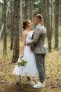 young couple bride in a white short dress and groom in a gray suit in a pine forest