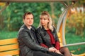 A young couple-brown-haired and blonde-sit on a bench and hold hands
