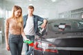 Young couple buying first electric car in the showroom. Woman charging ecological hybrid car with the power cable supply
