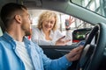 Young couple buying new car. Woman shows key to new auto to her husband who is sitting in car at dealership. Royalty Free Stock Photo