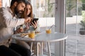 Young couple at cafe, she is drinking juice, he is showing her something in his mobile phone. They are happy Royalty Free Stock Photo
