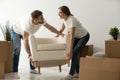 Young couple carrying chair together, placing furniture in new h