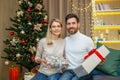 A young couple celebrating Christmas at home. They are sitting on the sofa with gifts in their hands Royalty Free Stock Photo