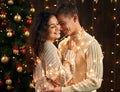 Young couple is in christmas decoration and lights, fir tree on dark wooden background, new year holiday concept Royalty Free Stock Photo