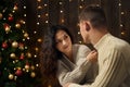 Young couple in christmas lights and decoration, dressed in white, fir tree on dark wooden background, winter holiday concept Royalty Free Stock Photo