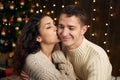 Young couple in christmas lights and decoration, dressed in white, fir tree on dark wooden background, winter holiday concept Royalty Free Stock Photo