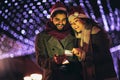 Couple in the city centre with holiday`s brights in background using phone Royalty Free Stock Photo