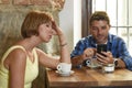 Young couple at coffee shop with internet and mobile phone addict man ignoring frustrated woman Royalty Free Stock Photo