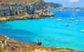 Young couple are coming down towards Turquoise lagoon paradise beach Cala Rossa with people swiming on Favignana island in Sicily,