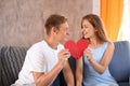 Young couple connecting halves of broken heart on sofa at home