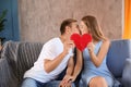 Young couple connecting halves of broken heart on sofa at home