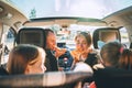 Young couple with daughters eating just cooked Italian pizza sitting in modern car with transparent roof. Happy family moments,