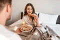 Young couple with delicious breakfast in the bed. Beautiful woman is eating fresh croissant with juice Royalty Free Stock Photo
