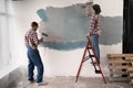 Young couple doing apartment repair together themselves, painting wall with paintbrush and paint roller. Family doing Royalty Free Stock Photo