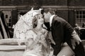 Young couple dressed in vintage costume relaxing with man on one knee, kissing on lawn in front of stately home Royalty Free Stock Photo
