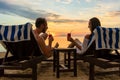 Young couple drinking cocktails on a beach at sunset during vacation