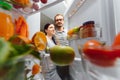 Young couple eating and looking at healthy fruit and vegetable in modern refrigerator. concept of healthy eating at home Royalty Free Stock Photo