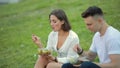 Young couple eating salad sitting on grass, picnic together