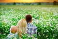 A young couple embraces outdoors in a field of daisies at sunset. Back to the camera. They watch the sunset