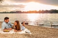 Young couple enjoying a picnic at the beach. Lying on the picnic blanket. White swans swimming the background Royalty Free Stock Photo