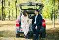 A young couple enjoying a serene moment, sipping beverages sitting in the trunk of their car, accompanied by a white Royalty Free Stock Photo