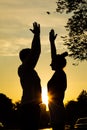 Young couple exercising on street in city from below view, sunset background. Darkened silhouettes of training man and Royalty Free Stock Photo