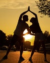 Young couple exercising on street near road in city from below view, sunset background. Darkened silhouettes of training Royalty Free Stock Photo