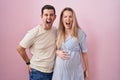 Young couple expecting a baby standing over pink background angry and mad screaming frustrated and furious, shouting with anger