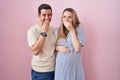 Young couple expecting a baby standing over pink background laughing and embarrassed giggle covering mouth with hands, gossip and Royalty Free Stock Photo