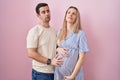 Young couple expecting a baby standing over pink background looking sleepy and tired, exhausted for fatigue and hangover, lazy