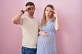 Young couple expecting a baby standing over pink background worried and stressed about a problem with hand on forehead, nervous