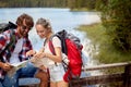 A young couple is exploring hiking map while taking a break beside the lake. Trip, nature, hiking