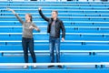 Young couple the fans cheer on team on empty stadium sector at match. Man and woman wave hands while standing together