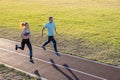 Young couple of fit sportsmen boy and girl running while doing exercise on red tracks of public stadium outdoors Royalty Free Stock Photo