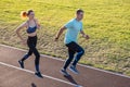 Young couple of fit sportsmen boy and girl running while doing exercise on red tracks of public stadium outdoors Royalty Free Stock Photo