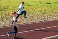 Young couple of fit sportsmen boy and girl running while doing exercise on red tracks of public stadium outdoors Royalty Free Stock Photo