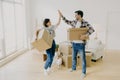 Young couple five high five to each other, carry big cardboard boxes during moving day, agree to work as team, pose in new