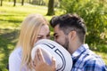 Young couple flirting and kissing behind a hat on a park bench Royalty Free Stock Photo