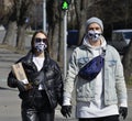 A young couple in funny protective masks and black gloves cross the road