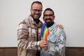 A young couple of gay men. The marriage is happy and they embrace looking at the camera with the gay pride flag in their hands. Royalty Free Stock Photo