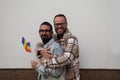 A young couple of gay men. The marriage is happy and they embrace looking at the camera with the gay pride flag in their hands. Royalty Free Stock Photo