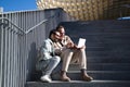 A young couple of gay men are sitting on the stairs with the laptop looking and pointing at the screen. The couple is having fun Royalty Free Stock Photo