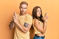 Young couple of girlfriend and boyfriend hugging and standing together holding symbolic gun with hand gesture, playing killing