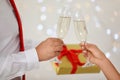 Young couple with glasses of champagne and gift box against blurred festive lights. Christmas celebration Royalty Free Stock Photo