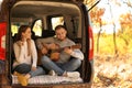 Young couple with guitar sitting in open car trunk