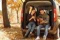 Young couple with guitar sitting in open car trunk