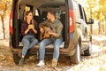 Young couple with guitar sitting in open car trunk