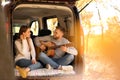 Young couple with guitar sitting in open car trunk