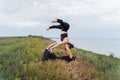 Young couple guy and girl doing acro yoga on the background of the sea. Man lying on the grass and balancing woman on his legs. Royalty Free Stock Photo