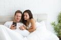 Young couple handsome husband and his beautiful wife just woke up in bed watching photoes on smartphone early in the Royalty Free Stock Photo